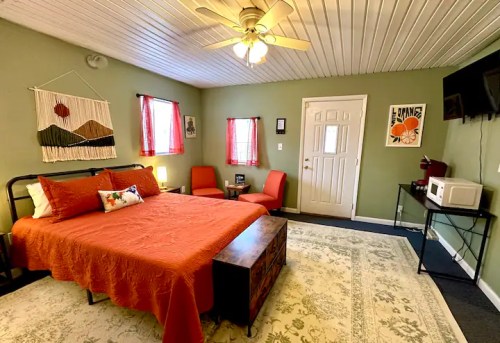 Cozy bedroom with a queen bed, two chairs, a TV, and decorative wall art in warm colors.