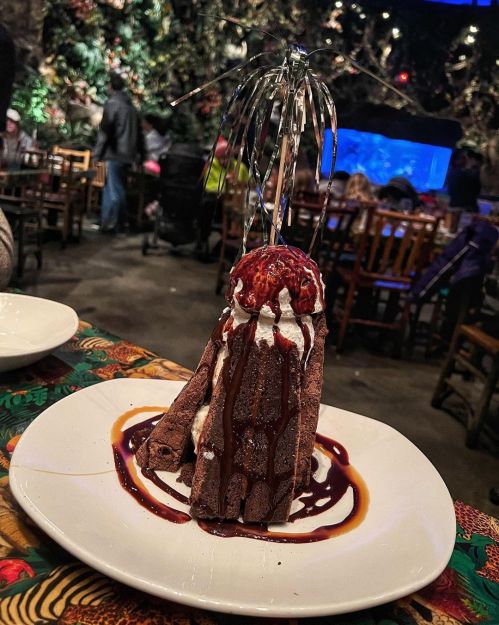 A chocolate dessert resembling a volcano, topped with whipped cream, a cherry, and drizzled with chocolate sauce.