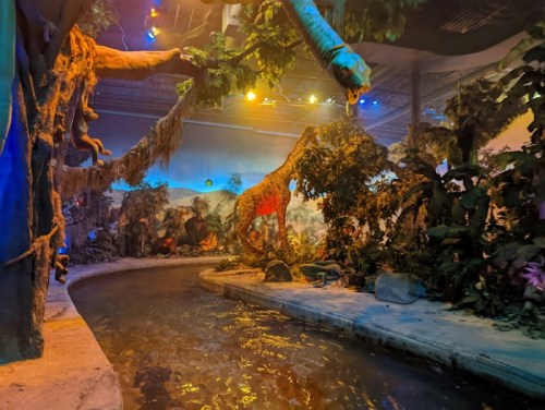 A lush indoor jungle scene with a winding river, vibrant plants, and colorful lighting creating a tropical atmosphere.