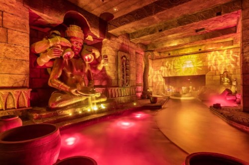 A mystical indoor space featuring a large statue with multiple arms, glowing lights, and a winding waterway.