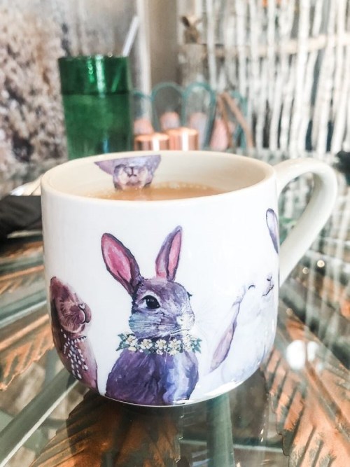 A decorative mug featuring illustrated rabbits, filled with a warm beverage, on a glass table.