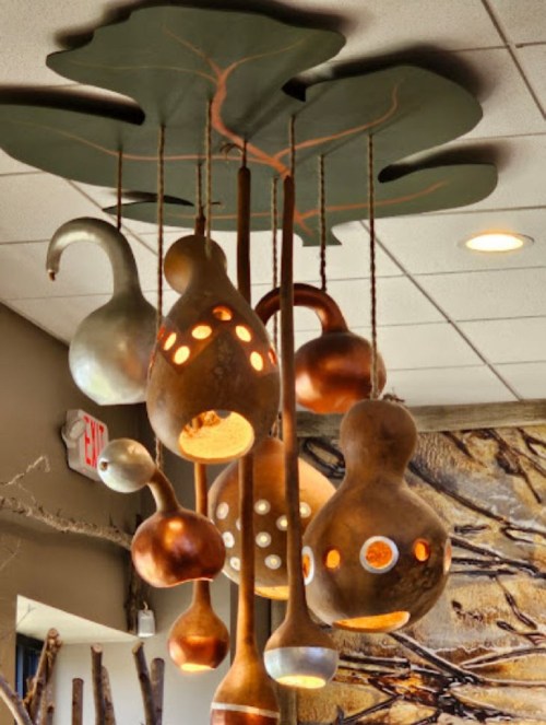 A unique ceiling installation featuring various decorative gourds with cut-out designs, hanging from a leaf-shaped base.