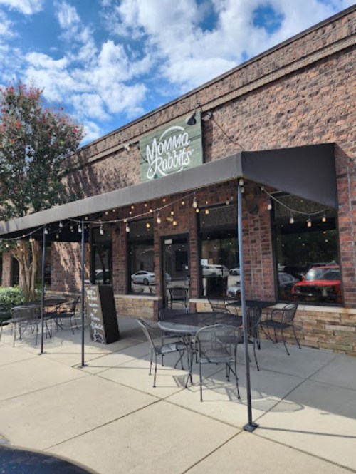 Exterior of Momma Rabbits restaurant with a patio, string lights, and a brick facade under a blue sky.