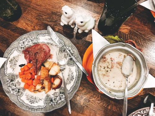 A plate with roast meat, carrots, and potatoes, alongside a bowl of creamy soup and two small salt shakers.