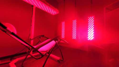 A dimly lit room with red LED light panels and a reclining treatment bed.