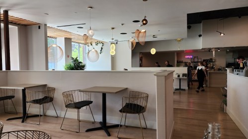 A modern restaurant interior with light wood floors, stylish seating, and decorative hanging lights.