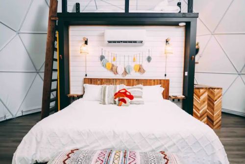 Cozy bedroom in a geodesic dome with a large bed, decorative wall hangings, and a wooden ladder.