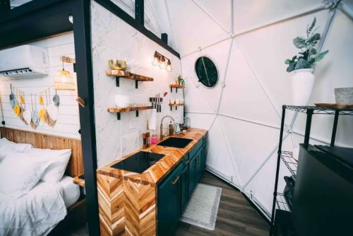Cozy kitchen in a geodesic dome, featuring wooden shelves, a double sink, and modern decor.