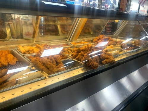 A display case filled with various fried foods, including chicken and egg rolls, in a food establishment.