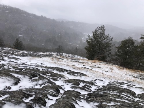 A snowy landscape with rocky terrain and trees, set against a misty, mountainous background.