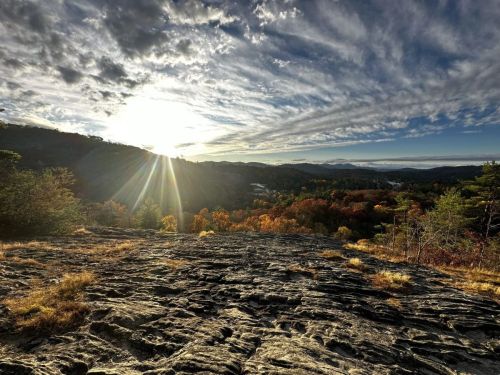 A scenic view of a rocky landscape at sunset, with vibrant autumn foliage and a dramatic sky filled with clouds.