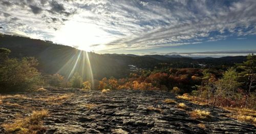 A scenic view of mountains and valleys at sunrise, with vibrant autumn foliage and dramatic clouds in the sky.