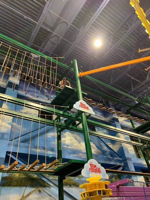 A child navigates a colorful indoor ropes course with various obstacles and platforms.