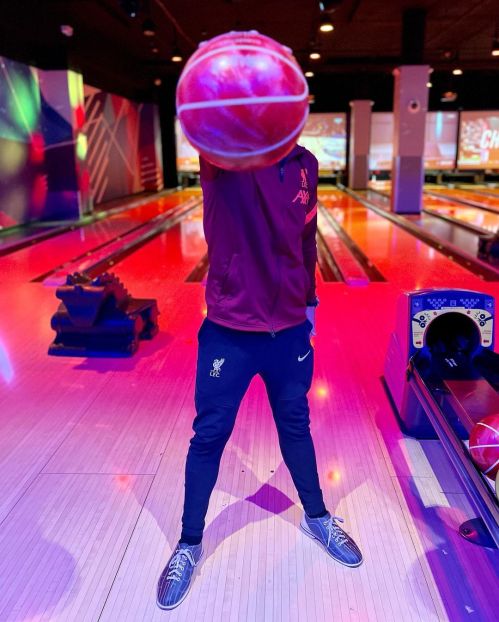 A person in sportswear holds a basketball above their head in a brightly lit bowling alley.
