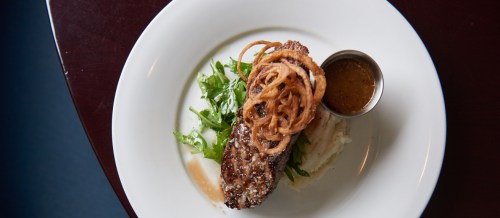 A plate featuring a breaded meat dish topped with crispy onions, served on a bed of mashed potatoes and greens.