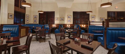 Cozy restaurant interior with blue booths, wooden tables, and warm lighting, featuring framed photos on the walls.