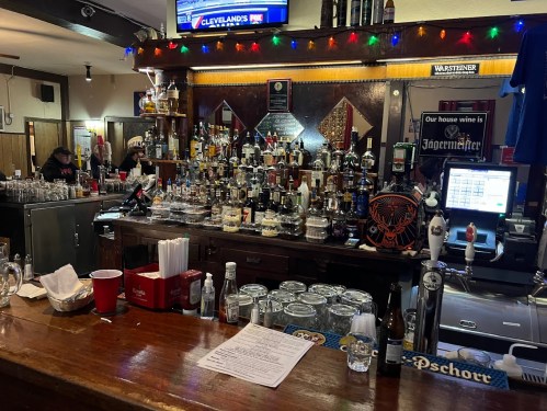 A bar counter filled with various bottles, glasses, and a menu, decorated with colorful lights.