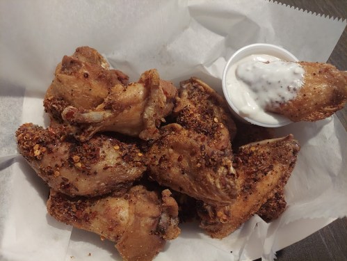 A plate of crispy, spicy chicken wings served with a small cup of ranch dressing on the side.