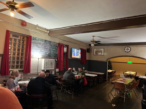 A cozy restaurant interior with tables, a TV showing news, and patrons enjoying their meals under warm lighting.
