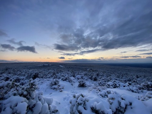 A snowy landscape at dusk, with clouds and a hint of sunset over a vast, serene horizon.