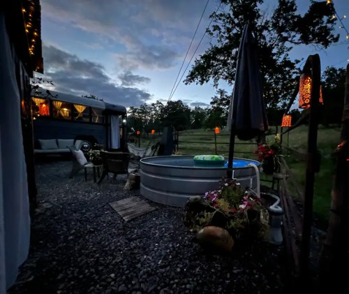 A cozy outdoor space at dusk featuring a metal pool, chairs, and decorative lights amidst a scenic landscape.