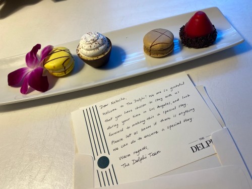 A plate with a macaron, cupcake, and dessert, alongside a welcome note from The Delphi Tavern.