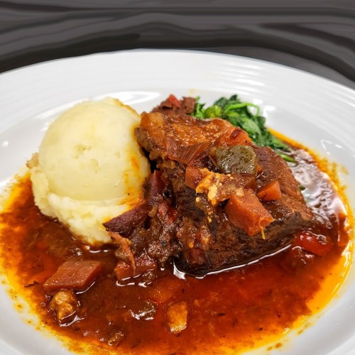 A plate of tender beef stew with rich gravy, served alongside creamy mashed potatoes and sautéed greens.