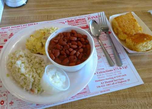 A plate with rice, coleslaw, red beans, and cornbread on a table with a menu underneath.