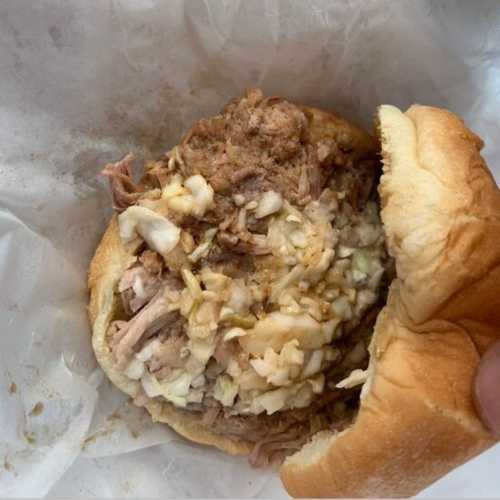 A close-up of a pulled pork sandwich with coleslaw on a soft bun, wrapped in paper.