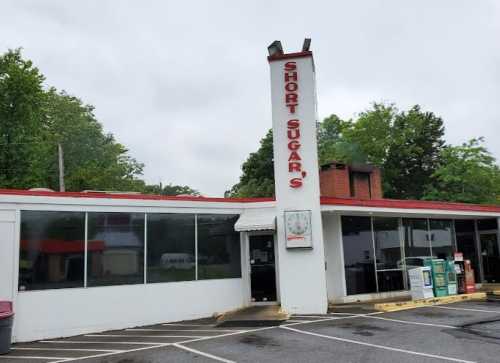 Exterior of Short Sugar's restaurant, featuring a red and white sign, large windows, and a cloudy sky.