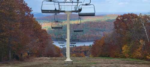 A ski lift towers over a colorful autumn landscape with trees and a lake in the background.