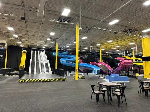 Indoor amusement park featuring colorful water slides and a large slide, with tables and chairs in the foreground.