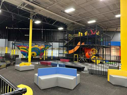 Indoor play area featuring colorful climbing structures, seating, and safety barriers. Brightly lit and spacious.