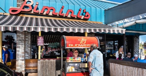 A colorful outdoor bar named Bimini's with patrons enjoying drinks and snacks on a sunny day.
