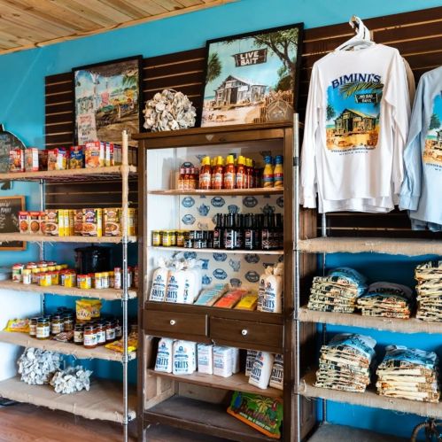 A colorful store interior featuring shelves of snacks, sauces, and apparel, with beach-themed decor on the walls.