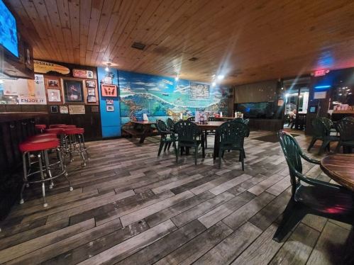 Interior of a casual restaurant with wooden floors, green chairs, and a mural of a beach scene on the wall.