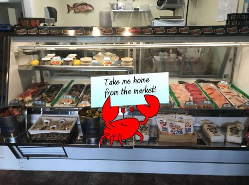 A seafood market display with various fish and shellfish, featuring a cartoon crab holding a sign that says, "Take me home!"