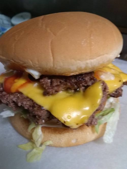 A close-up of a cheeseburger with two beef patties, melted cheese, lettuce, ketchup, and mayonnaise on a bun.