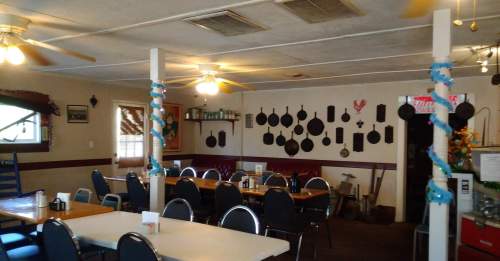 Cozy diner interior with wooden tables, chairs, and a wall decorated with cast iron cookware and country decor.