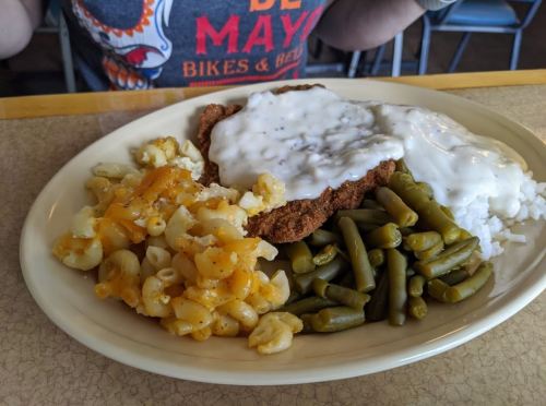 A plate of food featuring fried chicken with gravy, rice, green beans, and macaroni and cheese.