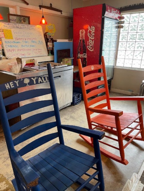 Two rocking chairs, one blue and one orange, sit in a cozy cafe with a Coca-Cola vending machine in the background.