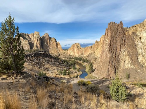 A scenic view of rugged cliffs and a winding river surrounded by dry grass and sparse trees under a blue sky.