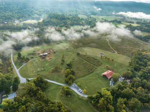 Aerial view of a lush green landscape with rolling hills, a red barn, and misty clouds hovering over the fields.