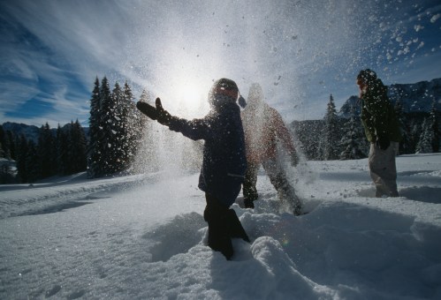 Children playing in the snow, throwing snowflakes into the air, with trees and mountains in the background.