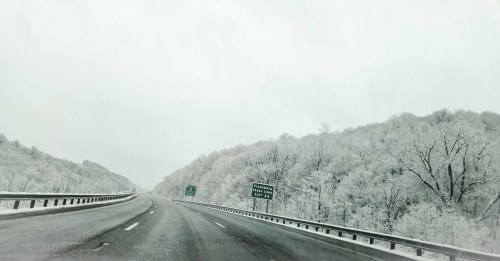 A snowy highway surrounded by frosted trees, with road signs indicating directions ahead.