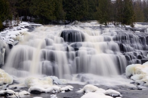 A cascading waterfall surrounded by icy rocks and trees, creating a serene winter landscape.