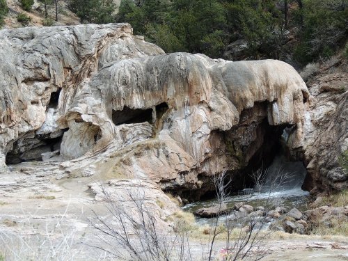 Rock formations with unique shapes near a flowing stream, surrounded by trees and natural landscape.