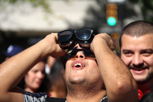 A person with sunglasses on their forehead looks up, smiling, while another person laughs in the background.