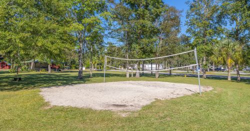 A sandy volleyball court surrounded by trees in a sunny park setting.