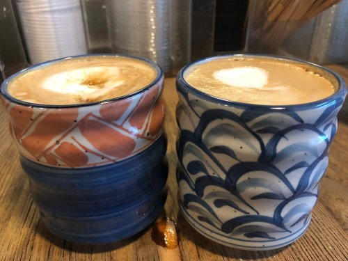 Two decorative coffee cups, one with a coral pattern and the other with a blue wave design, sit on a wooden table.